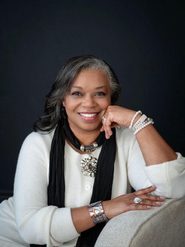 Smiling woman with silver-streaked hair wearing white and black, accessorized with jewelry.