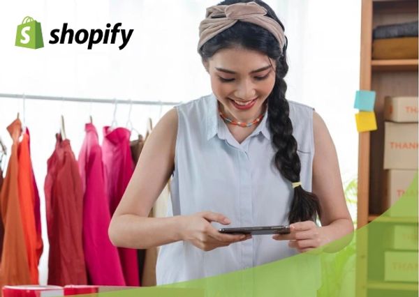 Woman using phone with Shopify logo and colorful clothes in background.