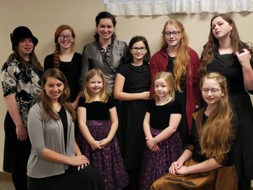 A group of girls and young women posing indoors in formal attire.