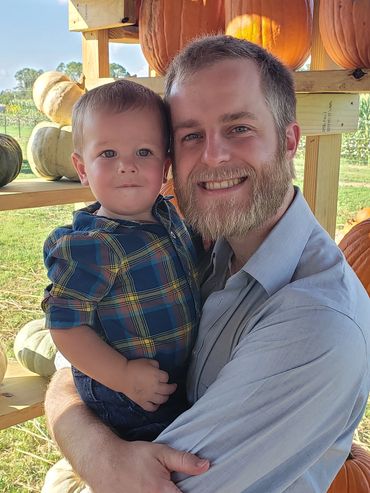Man holding toddler at a pumpkin patch on a sunny day.