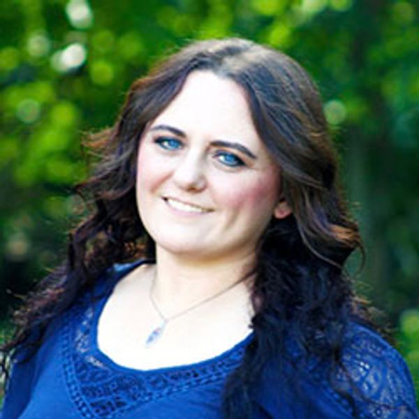 Woman with long dark hair smiling in a natural outdoor setting.