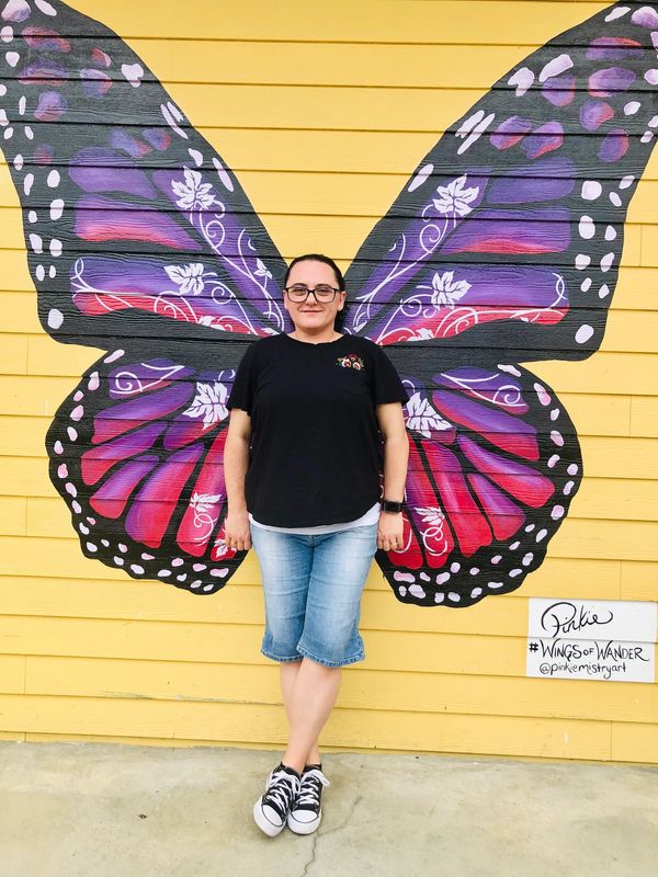 Person posing with butterfly wings mural on yellow wall.