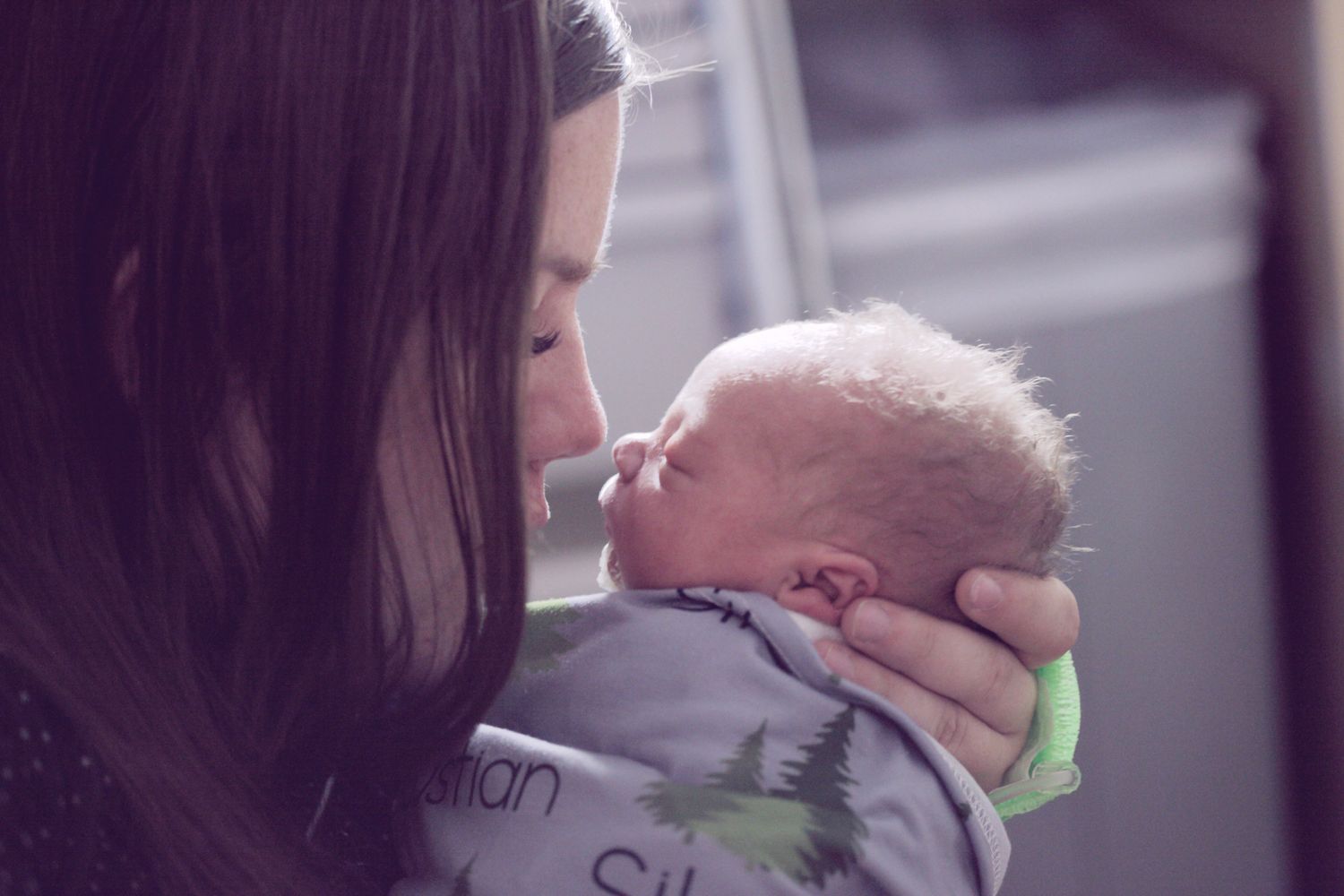 Closeup photo of parent with long brown hair nuzzling a newborn infant wrapped in a blue swaddle.