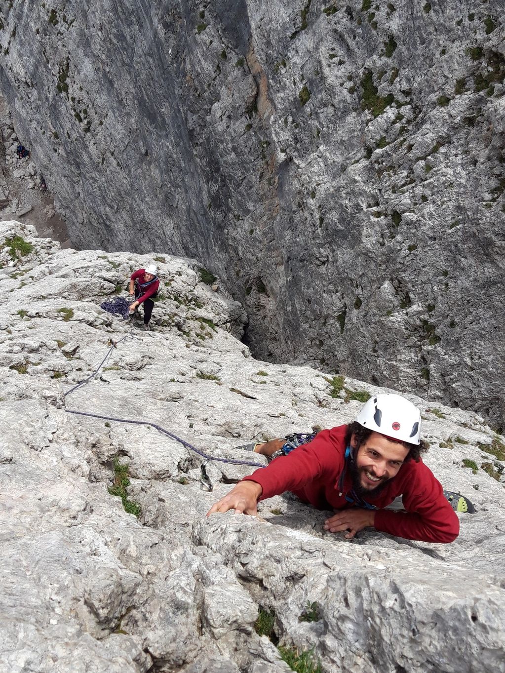 Two climbers ascending a steep rocky cliff, secured with ropes and helmets.