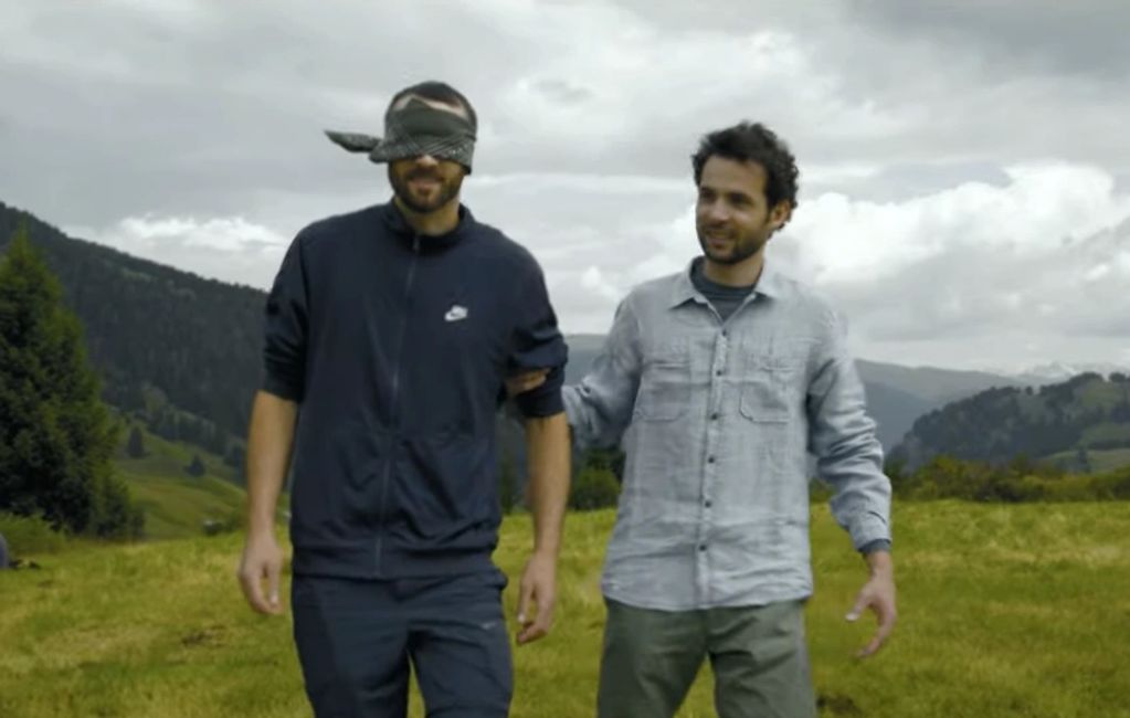 Two men outdoors, one blindfolded and guided by the other.