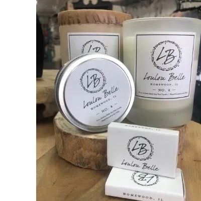 Loulou Belle scented candles and soap bars displayed on a wooden surface.