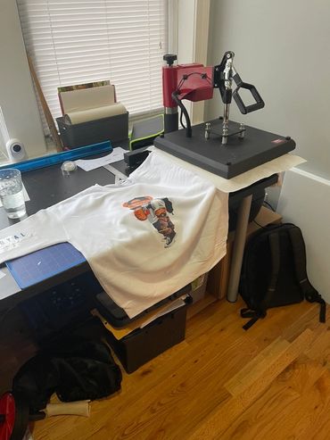Heat press machine printing a design on a white sweatshirt in a home setup.
