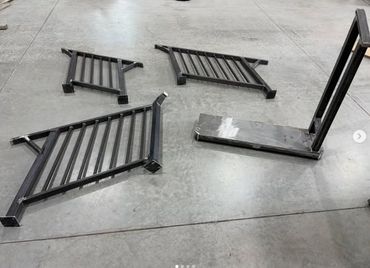 Four black metal frame pieces arranged on a concrete floor.