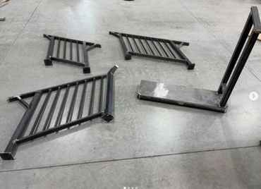 Four black metal frame pieces arranged on a concrete floor.