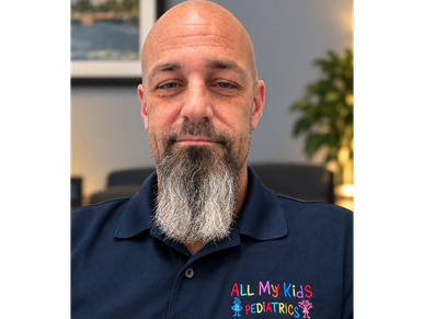 Man in navy blue pediatric shirt with colorful text and icons.