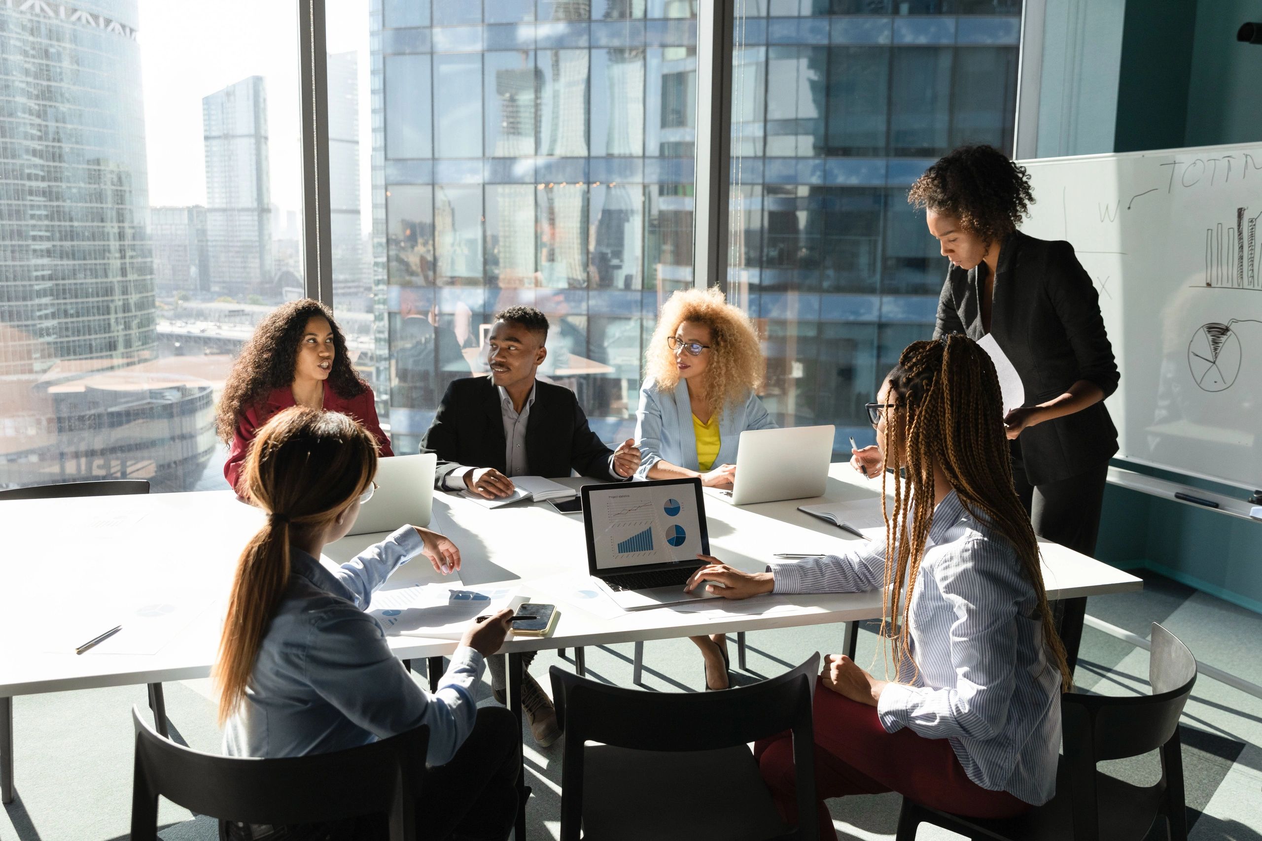A diverse group of professionals collaborates around a conference table with laptops