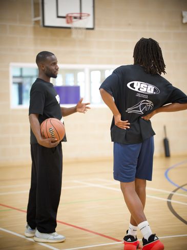 Two men talking in a gym holding a basketball.