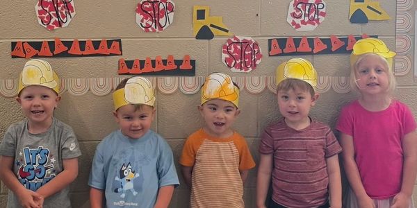 Five kids wearing paper construction helmets.