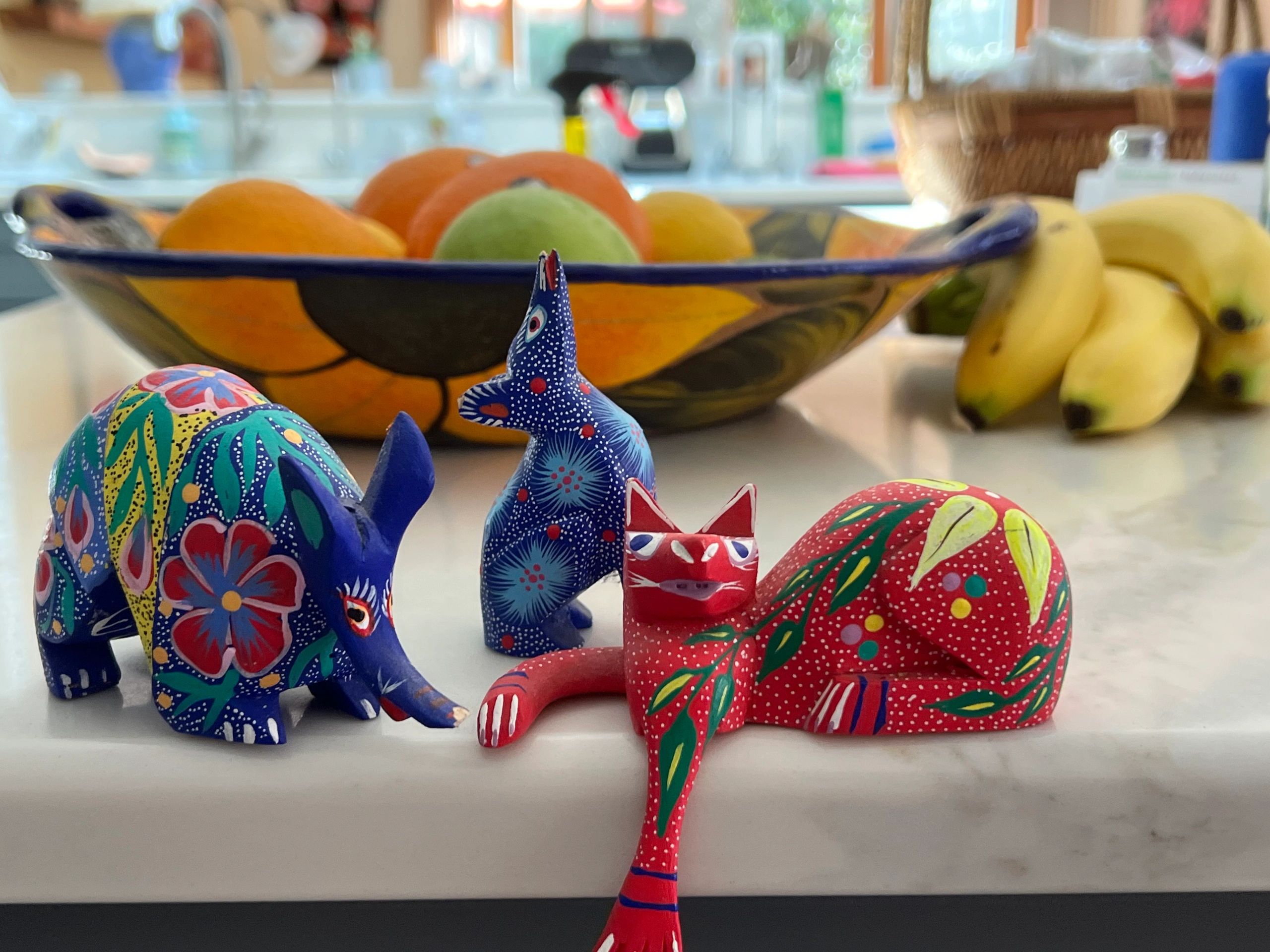 Three alebrijes, or painted, carved fantastical animals on a counter: a cat, coyote, and rhinocerous.