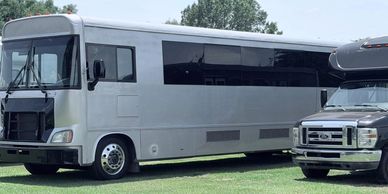 A large silver motorhome and a black vehicle parked on grass.