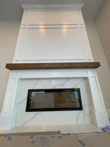 Modern fireplace with white paneling and a wooden mantel.