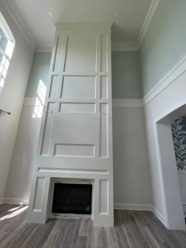 A tall white fireplace with detailed molding and light wood flooring.