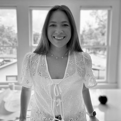 Smiling woman in a white lace blouse standing indoors near windows.