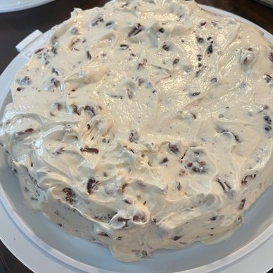 A homemade cake covered in creamy frosting with chocolate flakes.