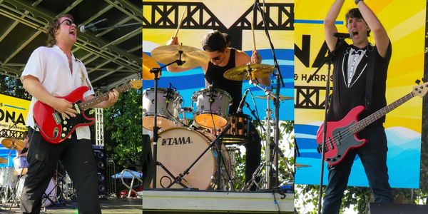 Three musicians playing guitar, drums, and bass at an outdoor event.