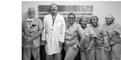 A diverse medical team posing happily in scrubs and lab coat.