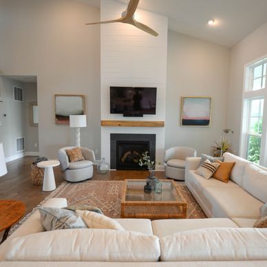 A living area with big windows on one side, a fire place, and long white couches
