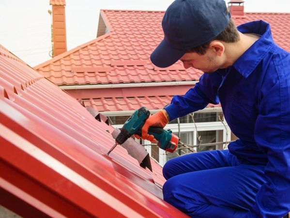 Young man worker in blue overall fix a metal tile roof with screwdriver