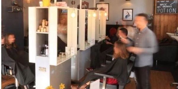 A hair salon with clients in chairs and stylists cutting hair.