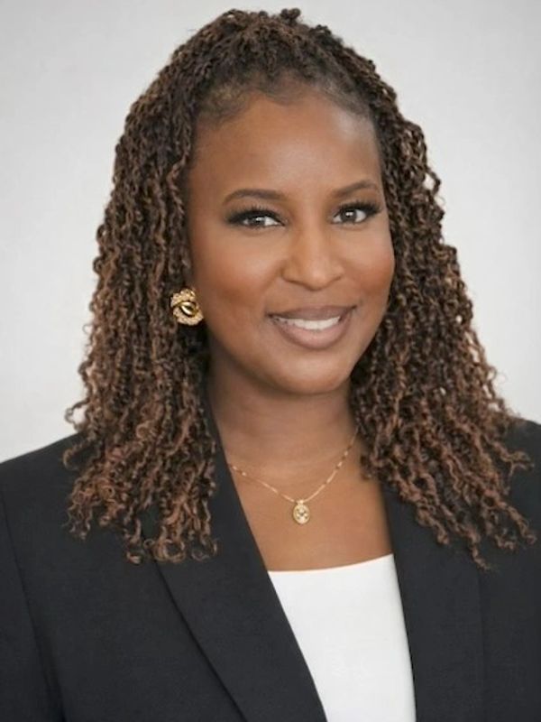 Professional woman with curly hair wearing a black blazer and gold jewelry.