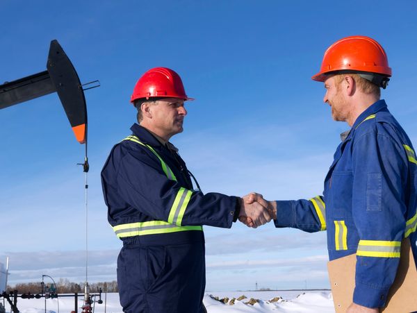 Two workers in helmets shaking hands at an oil extraction site.