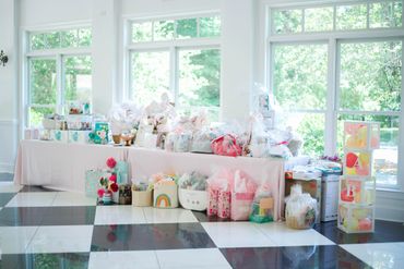 The table in a ballroom filled with Baby shower gifts.