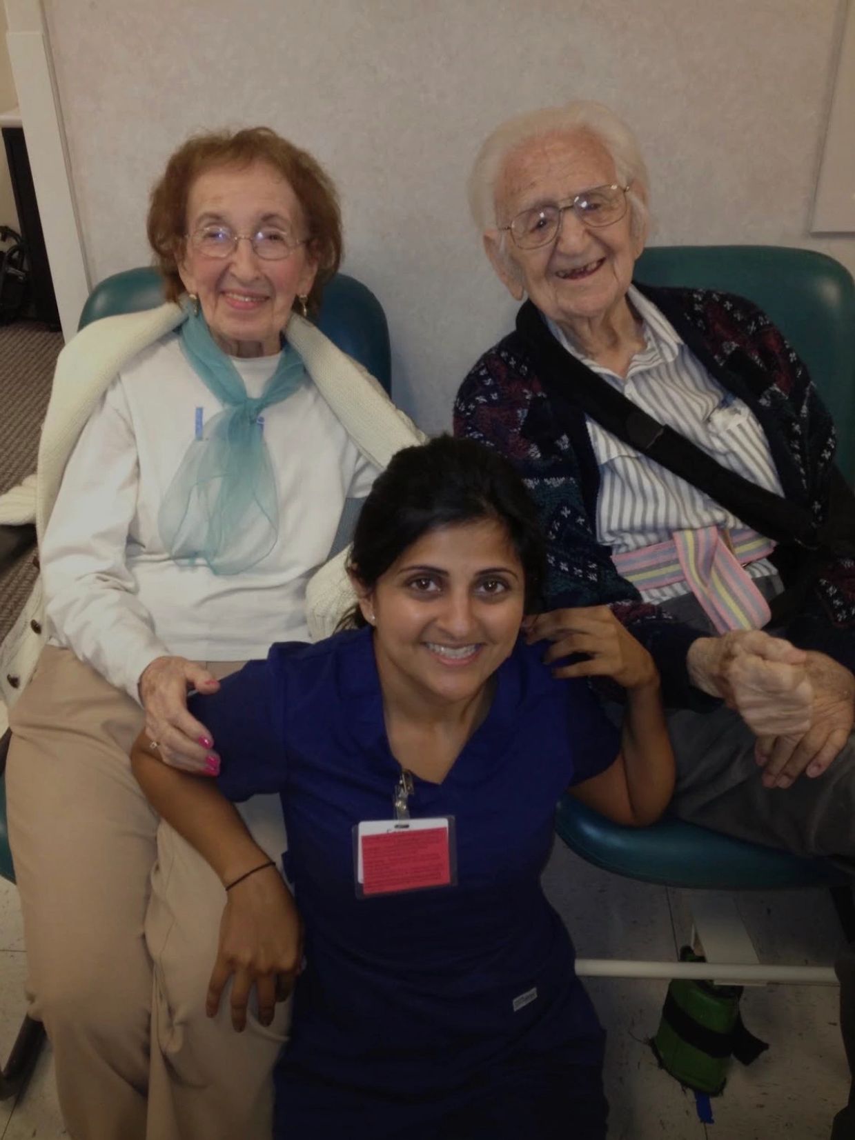 Two elderly people sitting with a smiling caregiver in front of them.