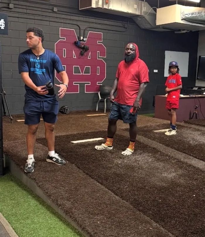 Three people standing on indoor pitching mounds in a sports training facility.