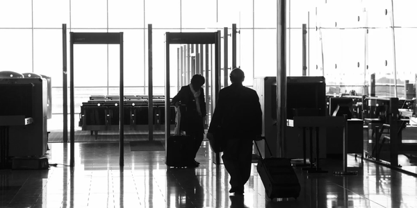Silhouetted travelers walk through an airport terminal with rolling suitcases.