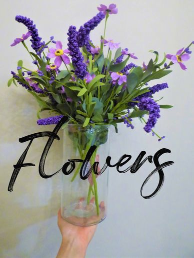 glass vase full of purple faux flowers against white background