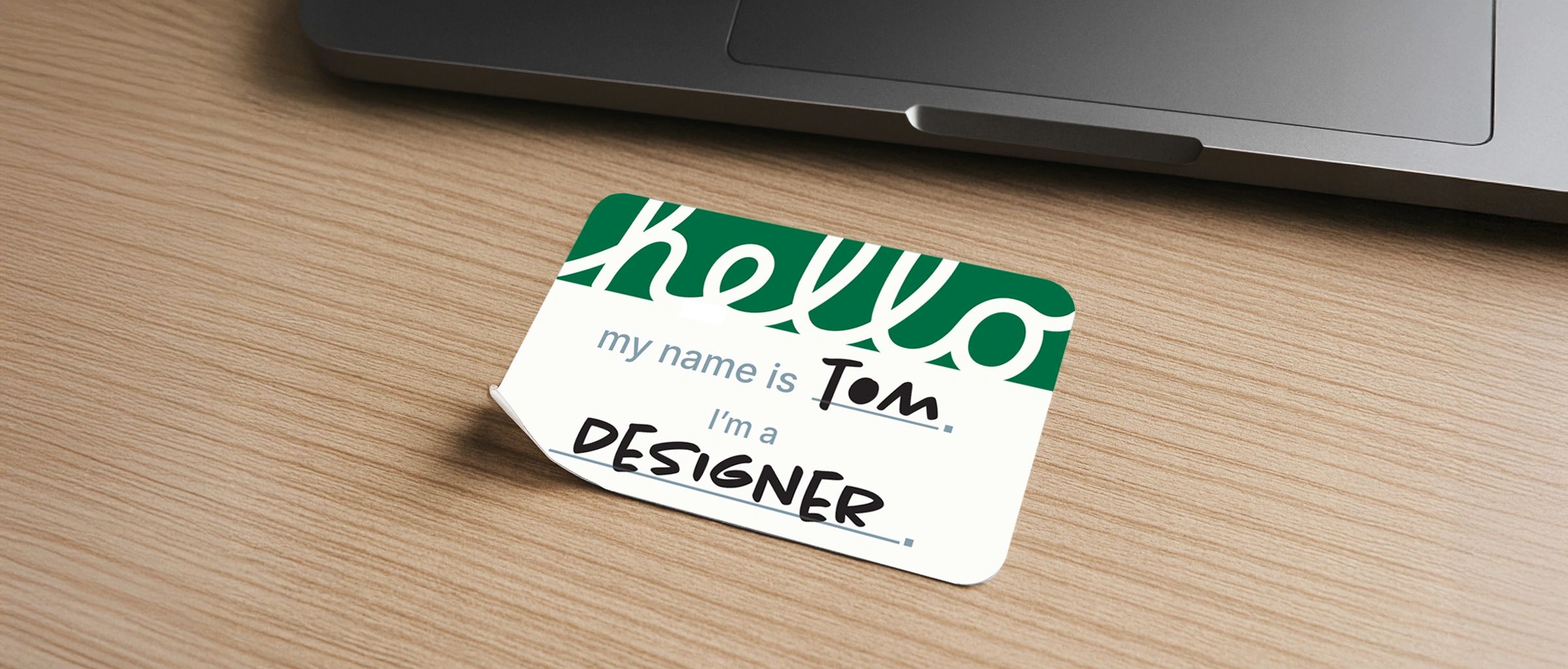 nametag on a desk with a laptop that says hello my name is tom and i'm a designer