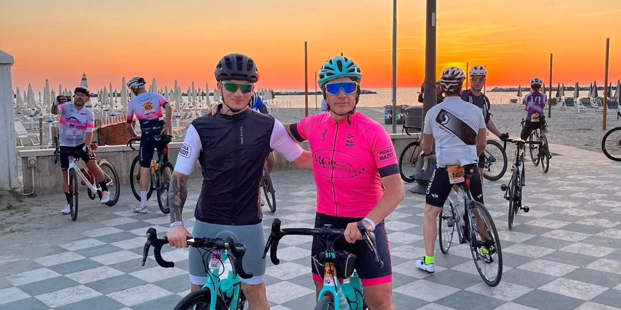 Due ciclisti si abbracciano al tramonto sul lungomare.