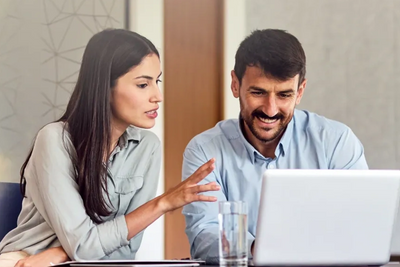Two colleagues discussing work while looking at a laptop screen.