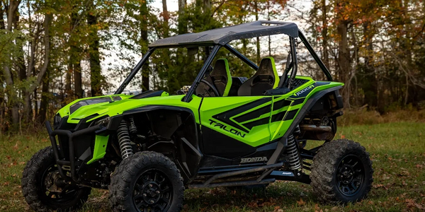 Bright green Honda Talon off-road vehicle parked on grass near autumn trees.