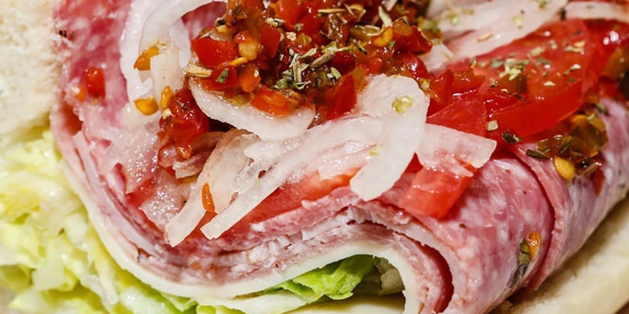 Close-up of a deli sandwich with salami, onions, tomatoes, and lettuce.