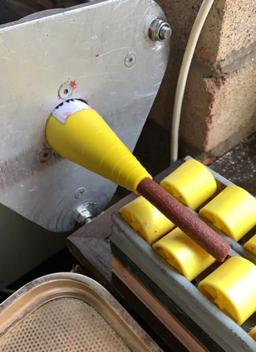 A yellow cone attached to a rusty rod on a mechanical device with yellow rollers.
