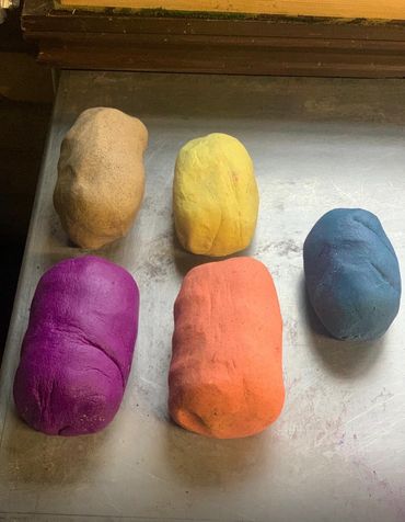 Five colorful clay or playdough lumps on a metal surface.