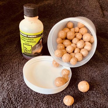 Fishing attractant bottle and bait balls spilling from a container on a towel.