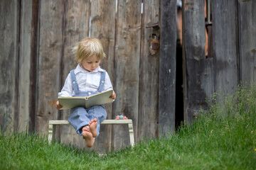 A young child loves reading a book on an outdoor bench.