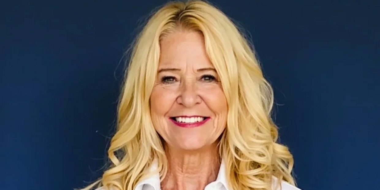 Smiling blonde woman in white shirt against blue background.