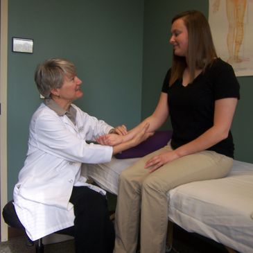 Photo of Sandra and a young woman patient sitting together while Sandra checks her pulse.