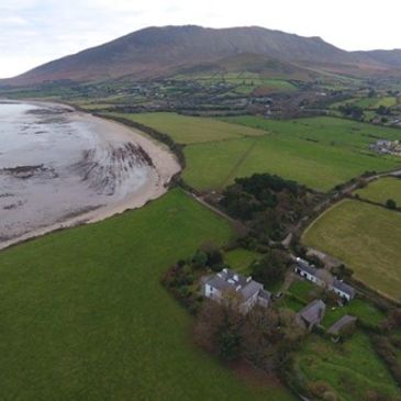 A scenic aerial view of green fields, a coastline, and a mountain in the background.
