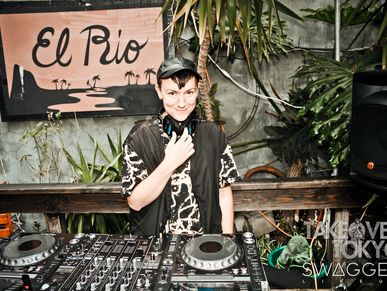 DJ smiling behind a mixer at El Rio with tropical plants around.