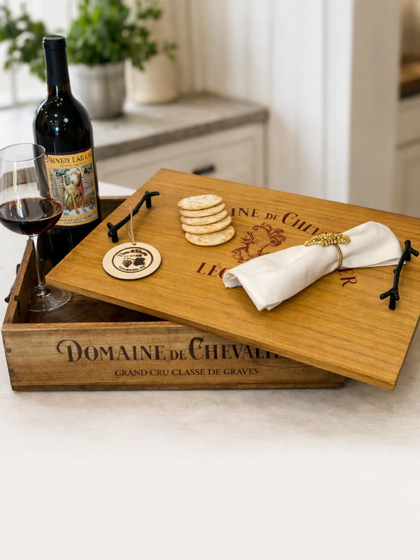 Rustic wine box with crackers, a napkin, and a glass of red wine on a kitchen counter.