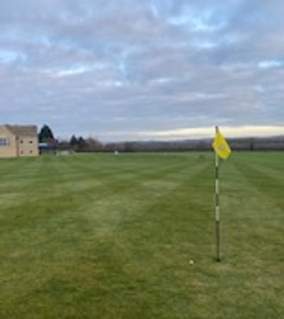 Golf course green with a yellow flag and cloudy sky.